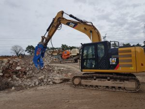 A Trevi Benne Fixed Secondary Pulveriser on a yellow excavator crushes concrete chunks into rubble for demolition.